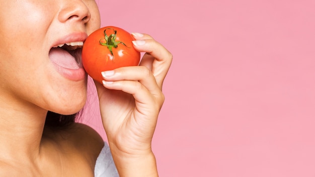 Donna del primo piano che mangia un pomodoro