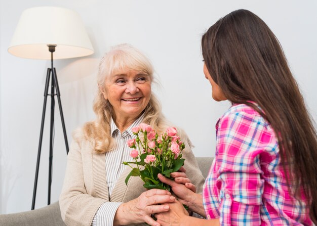 Close-up of woman giving pink flower roses bouquet to her senior mother