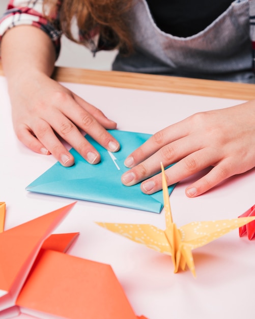 創造的な工芸品を作るための折り紙を折り畳む女性の手のクローズアップ