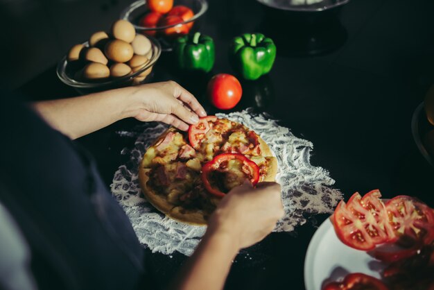 Close up of woman hand put topping on homemade pizza.