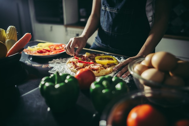 Close up of woman hand put topping on homemade pizza.