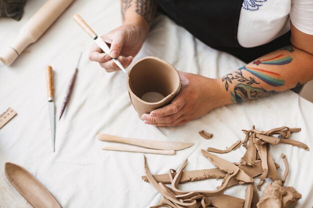 Close up woman hands with colorful tattoo working with clay and creating shape of vase at pottery studio