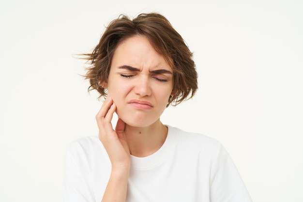 Close up of woman has a toothache touches her teeth and frowns from painful discomfort stands over