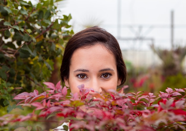 温室の植物の後ろに隠れているクローズアップの女性