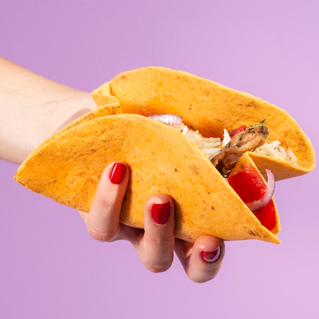 Close-up woman holding burrito with purple background