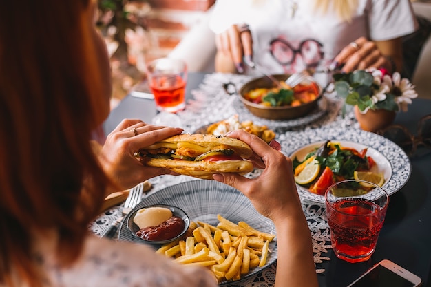 Close up of woman holding chicken sandwich served with fries and sauces