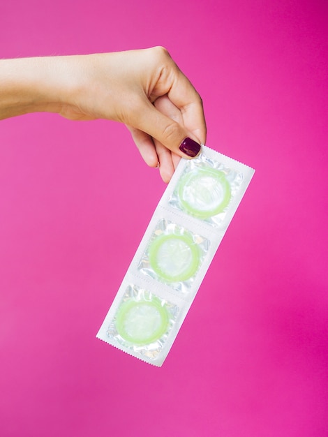 Free photo close-up woman holding condoms with pink background