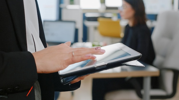 Close up of woman holding digital tablet with touch screen for business project. Woman with corporate job using modern gadget to work on management and marketing strategy in office.