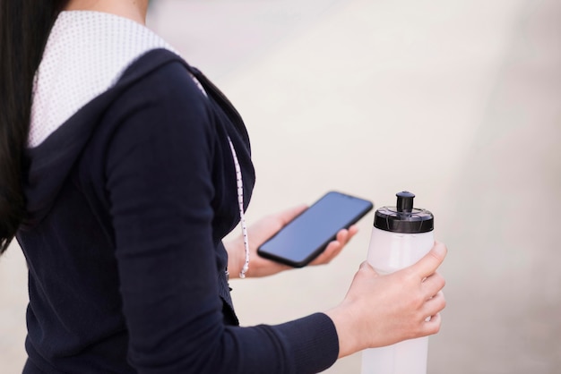 Женщина конца-вверх держа мобильный телефон и бутылку с водой