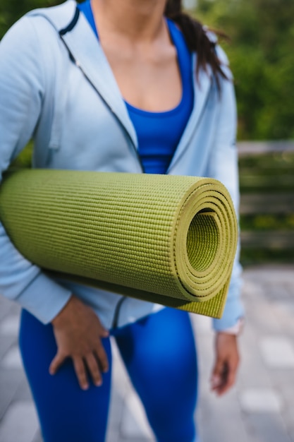 Close-up woman holding roll fitness or yoga mat after working out in the park.