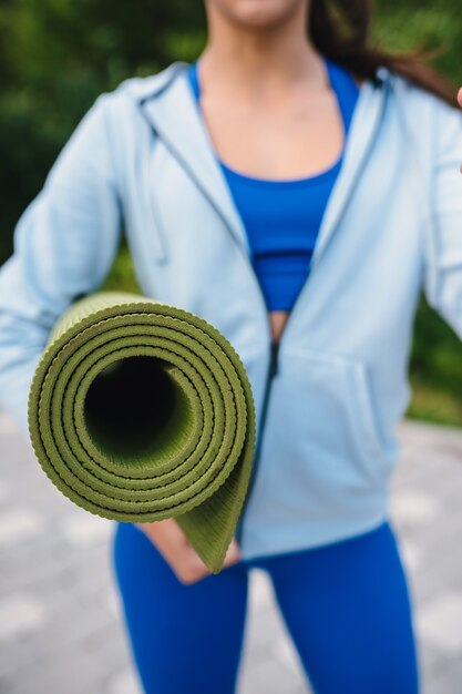 Close-up woman holding roll fitness or yoga mat after working out in the park.