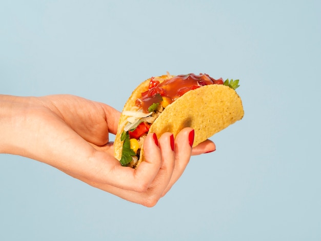 Close-up woman holding taco with blue background