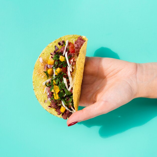 Close-up woman holding taco with green background