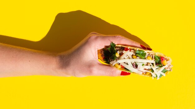 Close-up woman holding taco with yellow background