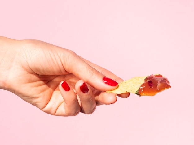 Close-up woman holding tortilla chips with pink background