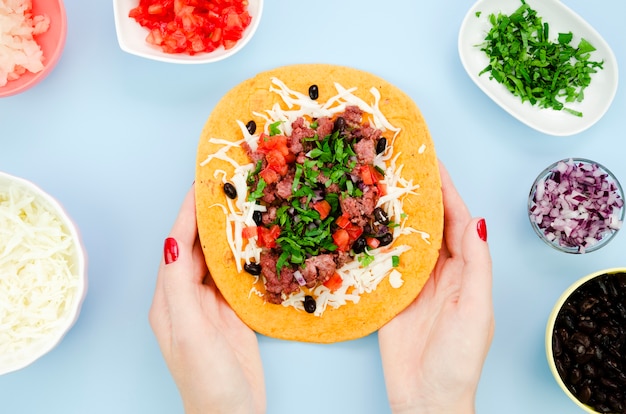 Close-up woman holding unfolded burrito with blue background