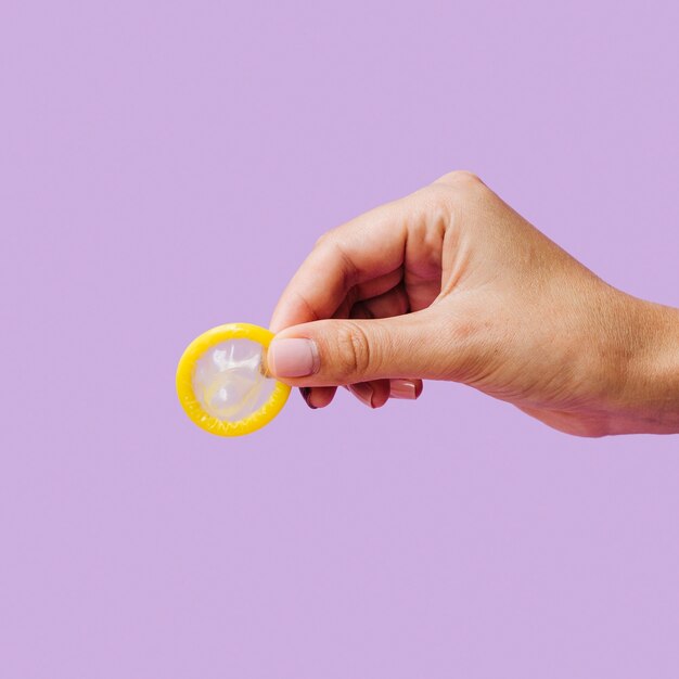 Close-up woman holding unwrapped yellow condom