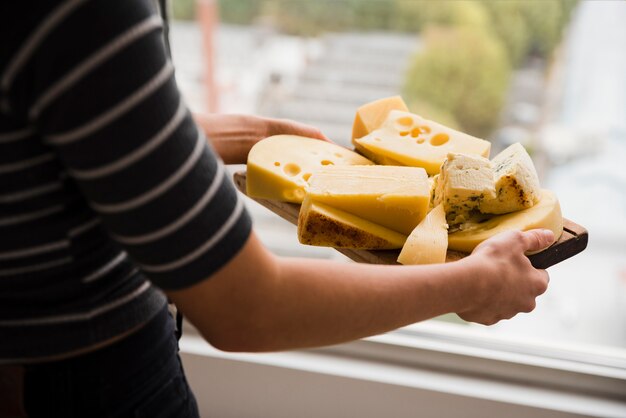 Close-up of a woman holding wooden chopping board with cheese slices