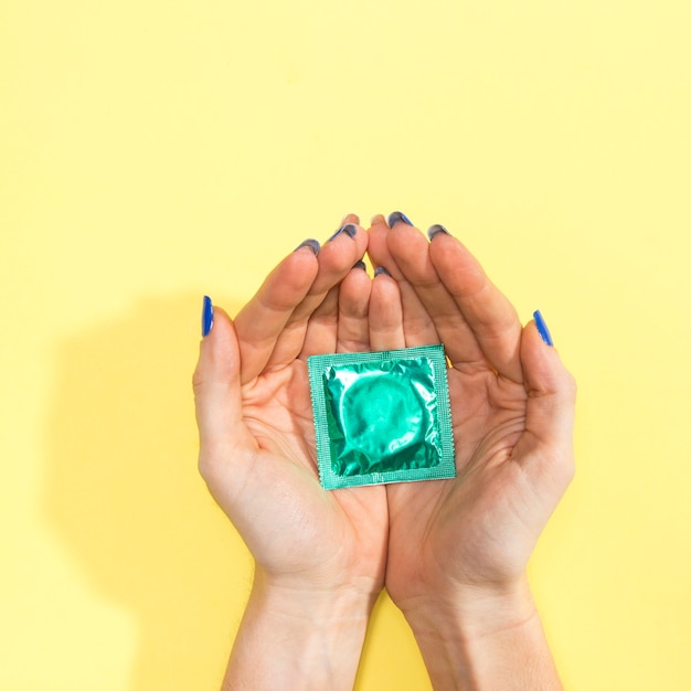 Close-up woman holding a wrapped green condom 