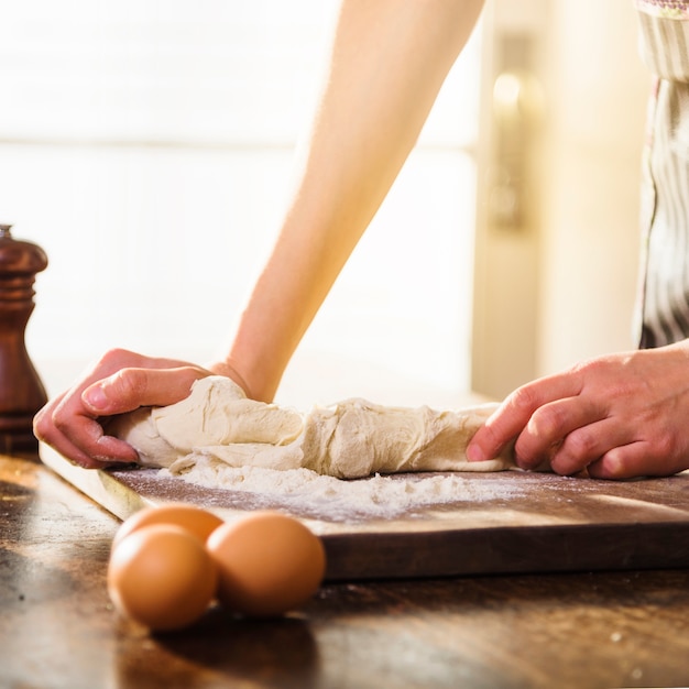 Close-up of woman kneading the dough on chopping wooden board