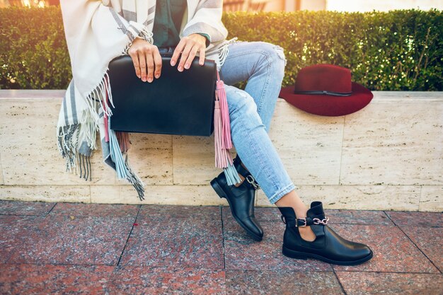 黒革のブーツ、ジーンズ、靴の春のトレンド、バッグを保持している女性の足のクローズアップ
