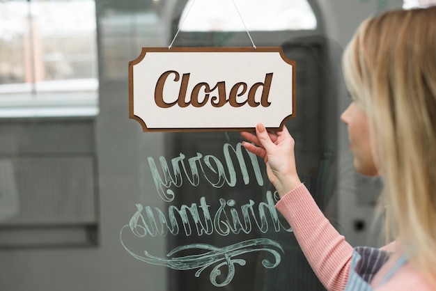 Close-up of a woman looking at closed tag hanging on a glass of storefront