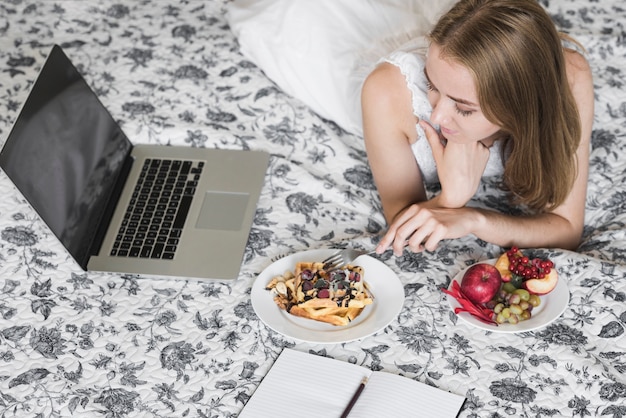 Крупным планом женщины, глядя на ноутбук, едят вафли с ягодами на цветочные кровати