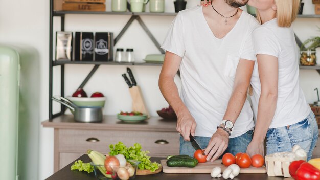 Close-up of woman loving her boyfriend cutting red tomato with knife in kitchen