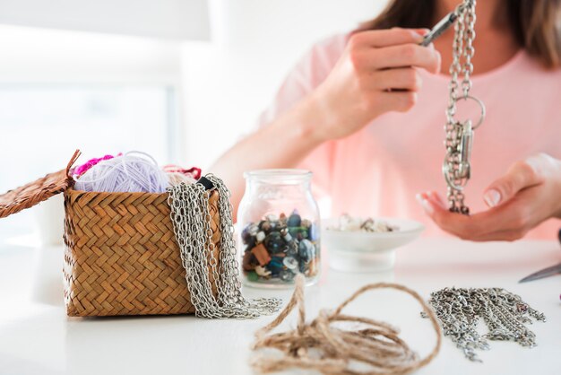 Close-up of a woman making the chain and bracelet with beads on white desk