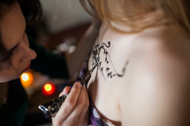 Close-up of a woman making a heena tattoo from female artist