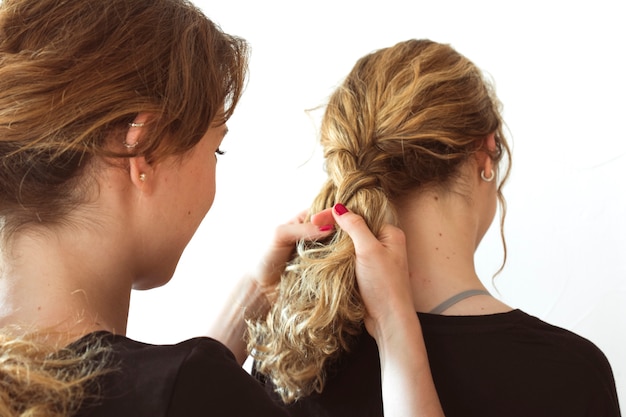 Close-up of woman making her sister's braid against white background