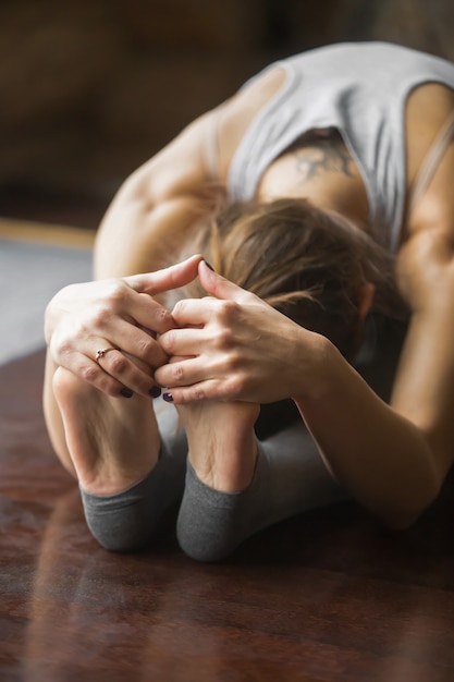 Chiuda in su della donna nella posa di paschimottanasana