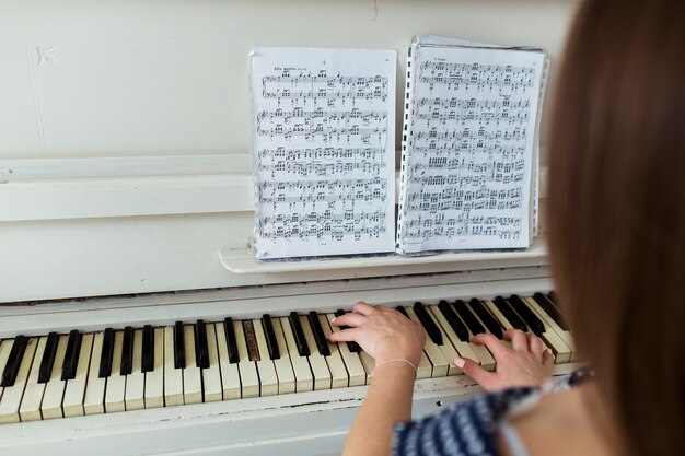 Крупным планом женщина играет на пианино, глядя на музыкальный лист на фортепиано