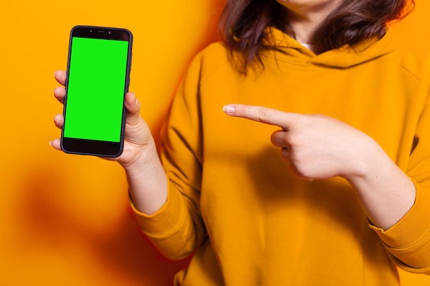 Primo piano di una donna che punta allo schermo verde verticale sul telefono. persona in possesso di modello di mockup isolato e sfondo con chiave cromatica sullo smartphone. adulto con cellulare sulla fotocamera