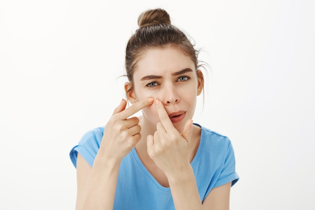 Close-up of woman popping pimple, removing acne from cheek