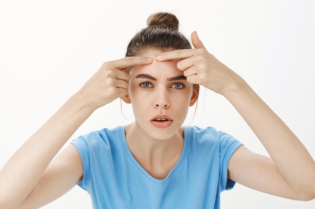 Free photo close-up of woman popping pimple, removing acne from forehead