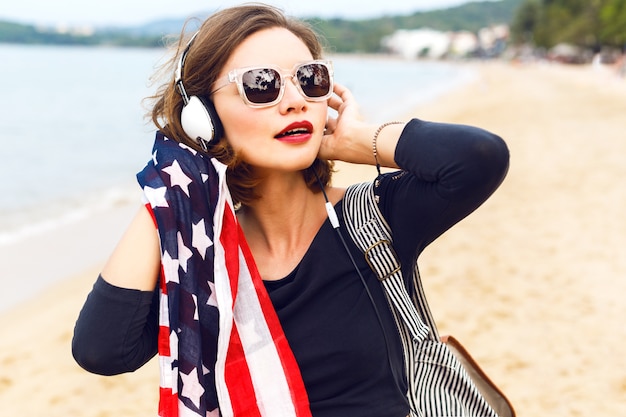 Free photo close up woman posing at the beach listening music in her stylish big headphones