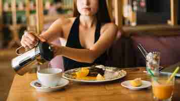 Foto gratuita primo piano del caffè di versamento della donna con il dessert sulla tavola nel caf���