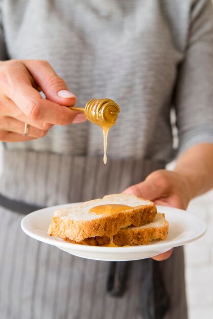 Close-up woman pouring honey ober bread slice