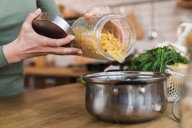 Close-up woman pouring pasta into cooking pot