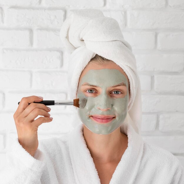Close-up woman putting on green face mask