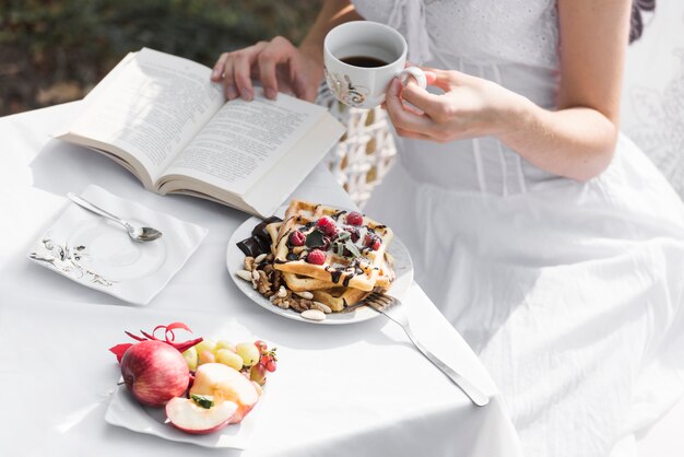 Крупным планом женщина читает книгу во время завтрака