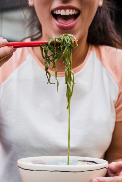 Close-up of a woman ready to eat green seaweeds with chopsticks