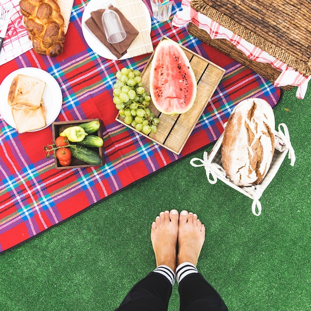 Foto gratuita il primo piano dei piedi della donna vicino allo spuntino di picnic su coperta