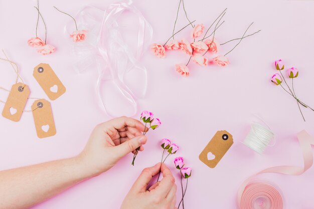 ピンクの背景にリボンとタグで花を生ける女性の手のクローズアップ