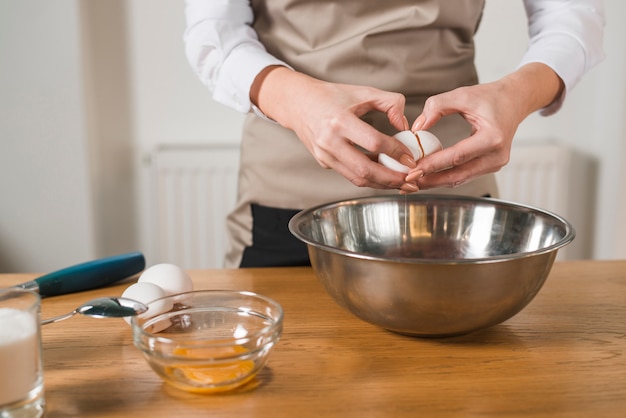 Close-up of woman's hand breaking an egg in the mixing bowl on wooden table