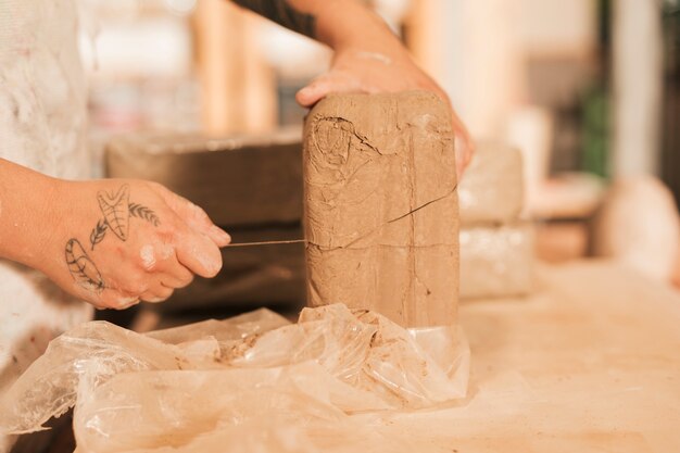 Close-up of woman's hand cutting the clay with thread on wooden table