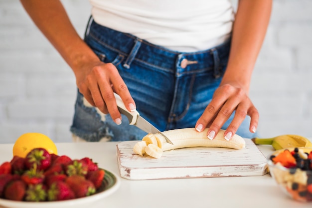 Close-up of woman's hand cutting ripe banana on board