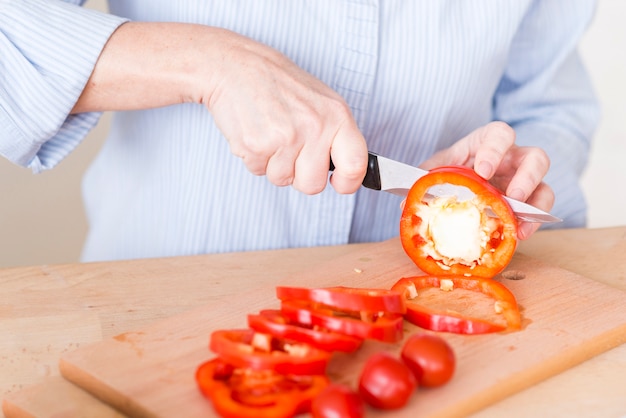 Close-up of woman's hand cutting the slice of red bell pepper with knife on chopping board