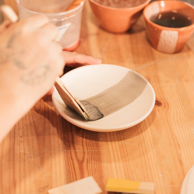 Close-up of woman's hand decorating dish in pottery workshop